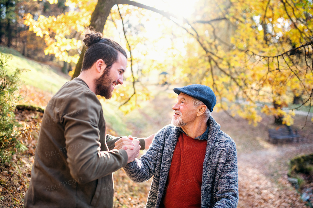 A senior father and his son walking in nature, shaking hands when talking.