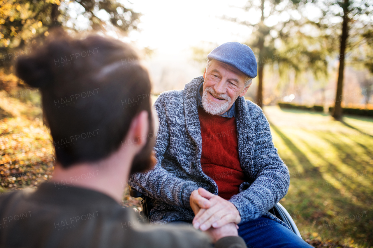 A senior father with wheelchair and his son on walk in nature, talking.