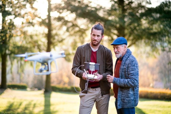 Senior father and his young son with drone in nature, talking.