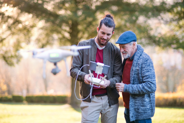 Senior father and his young son with drone in nature, talking.