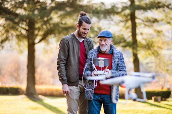 Senior father and his young son with drone in nature, talking.