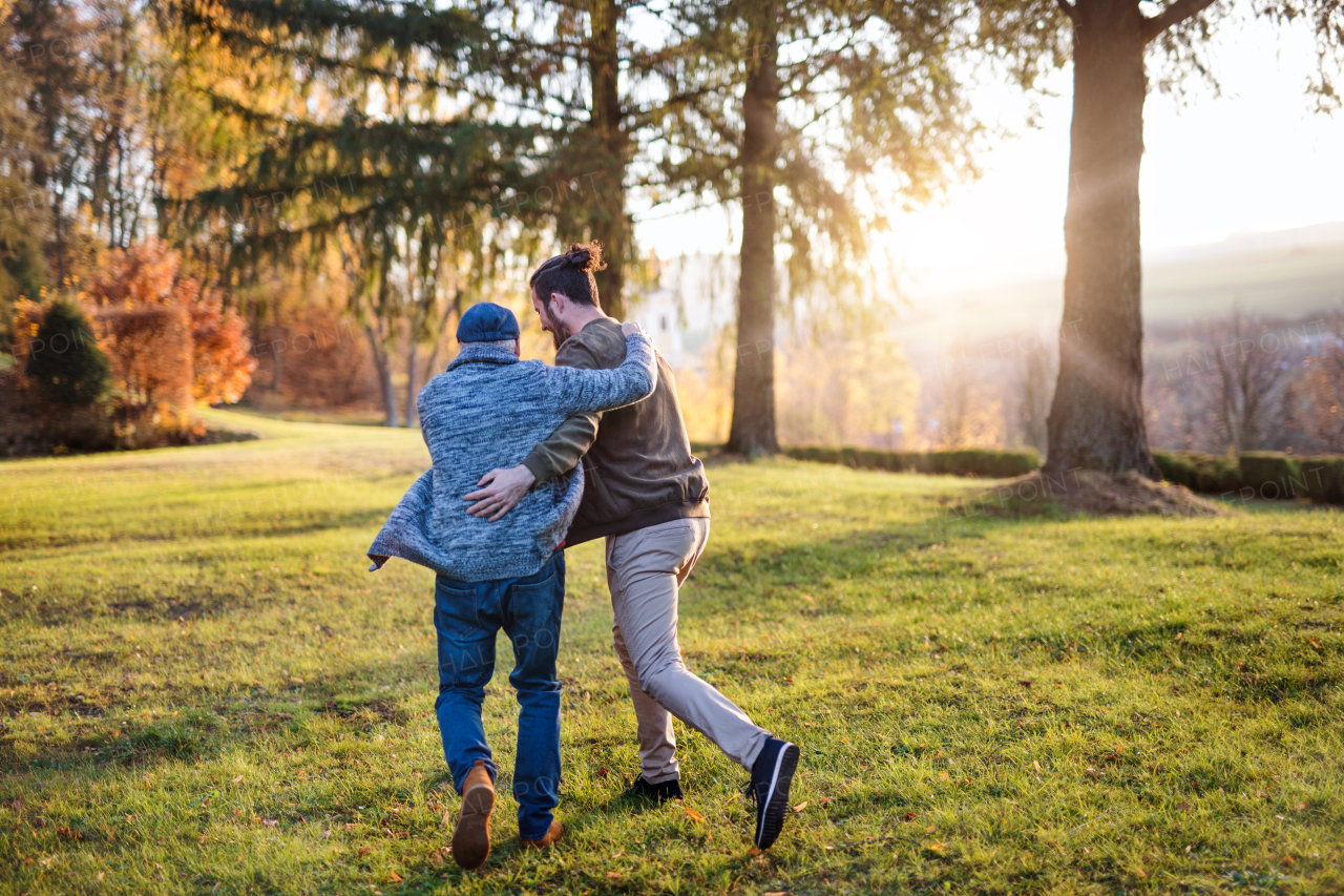 A rear view of senior father and his son on walk in nature, running.