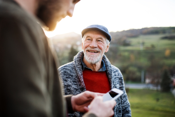 A young man and his senior father on a walk in nature, using smartphone.