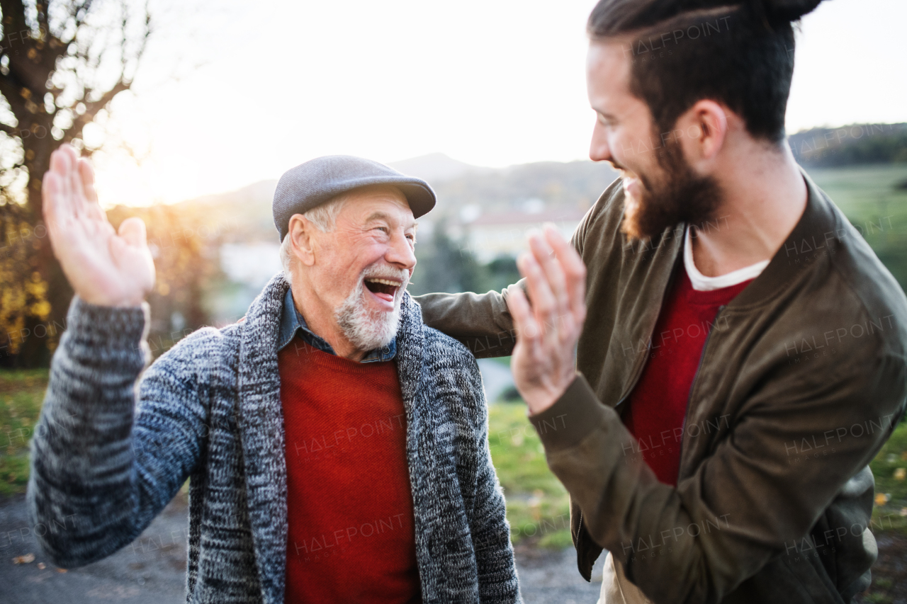 Laughing senior father and his young son on a walk in nature, giving high five.