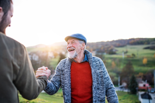 Laughing senior father and his young son on a walk in nature, shaking hands.