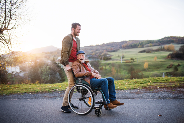 A young man and his senior father in wheelchair on a walk in town at sunset.