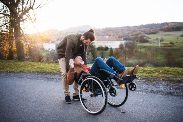 A young man and his senior father in wheelchair on a walk in town, having fun.