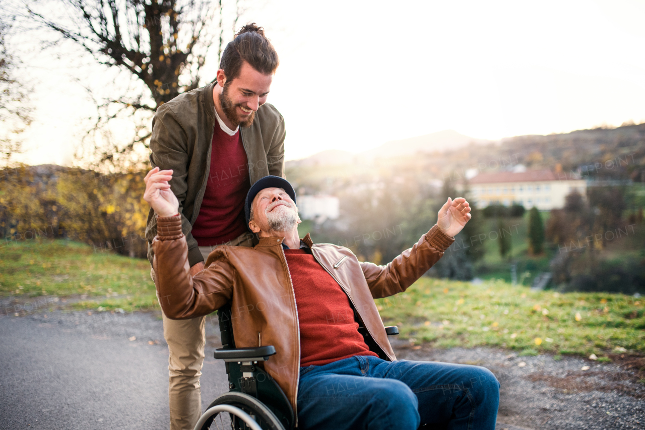 A young man and his senior father in wheelchair on a walk in town at sunset.