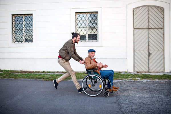 A young man and his senior father in wheelchair on a walk in town, having fun.