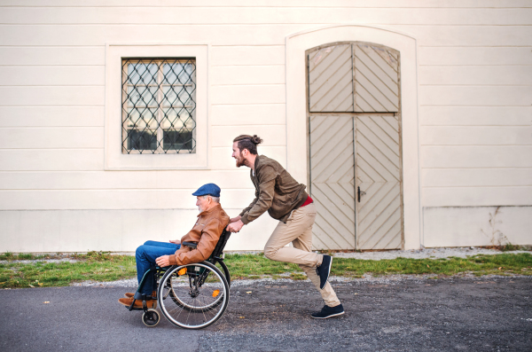 A young man and his senior father in wheelchair on a walk in town, having fun.