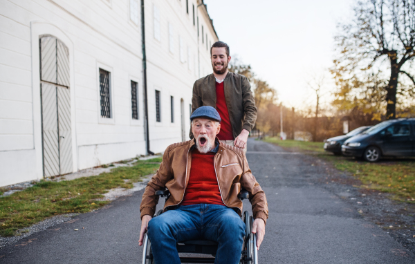 A young man and his senior father in wheelchair on a walk in town, having fun.