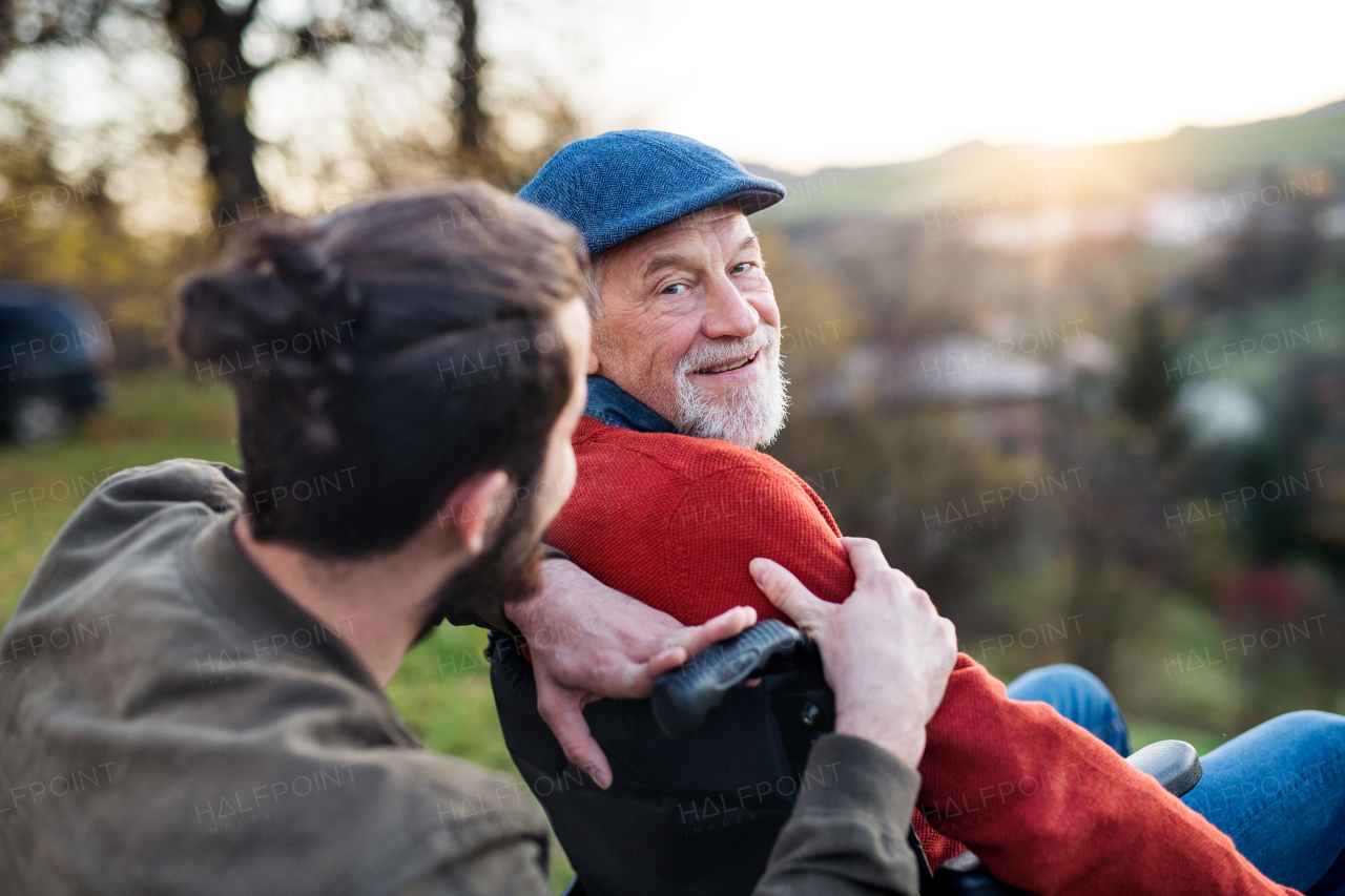 A senior father with wheelchair and his son on walk in nature, talking.