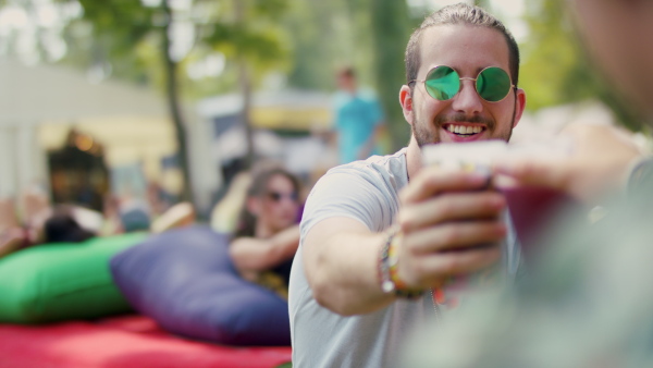 Front view of young man with sunglasses at summer festival, sitting.