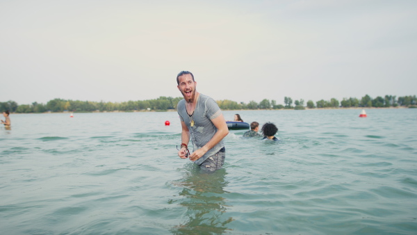 Young wet man having fun at summer festival, standing in lake. Copy space.