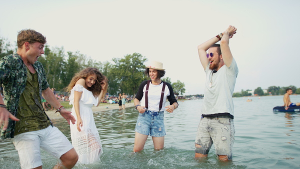 Group of young friends at summer festival, standing in lake and splashing water.