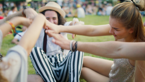 Group of cheerful young friends sitting on ground at summer festival, talking.