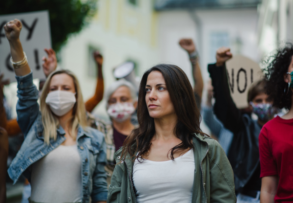 A group of people activists protesting on streets, demonstration and coronavirus concept.