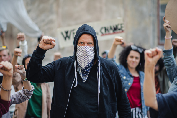 Portrait of mature man with group of people activists protesting on streets, demonstration and coronavirus concept.