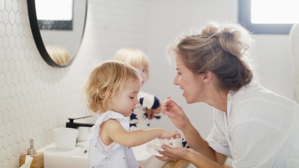 A young family with two small children indoors in bathroom, having fun in the morning or evening.