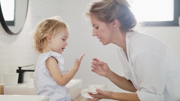 A young family with two small children indoors in bathroom, having fun in the morning or evening.