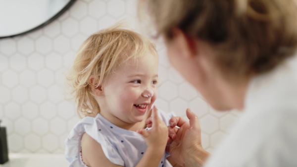 An unrecognizable young mother with small daughter indoors in bathroom, having fun.