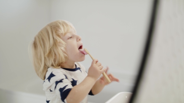 Small blond boy indoors in bathroom, brushing teeth and washing in the morning or evening.