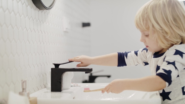 Small blond boy indoors in bathroom, brushing teeth and washing in the morning or evening.