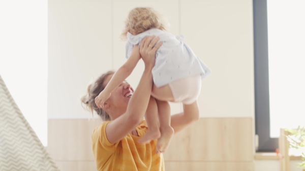 Cheerful young mother with small daughter indoors in bedroom playing and hugging.