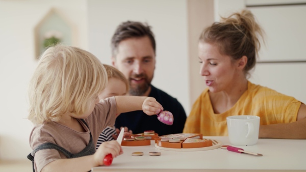 Young family with two small children indoors in bedroom playing with wooden toys.