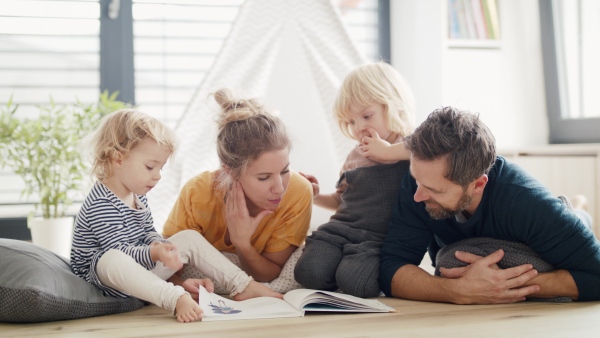 Front view of young family with two small children indoors in bedroom reading a book.