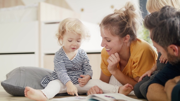 A young family with two small children indoors in bedroom reading a book.