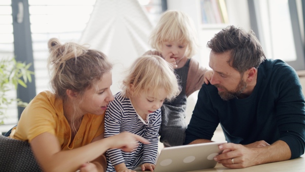 Front view of young family with two small children indoors in bedroom, using tablet.