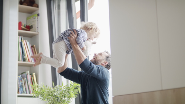 Cheerful young father with small daughter indoors in bedroom playing and hugging.