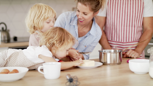 Front view of young family with two small children indoors in kitchen, preparing food.