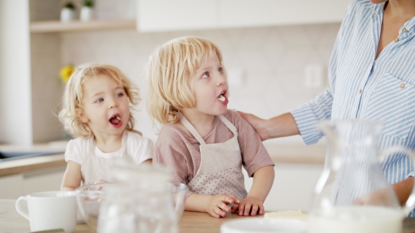 Front view of young mother with two small children indoors in kitchen, preparing food. Slow motion.