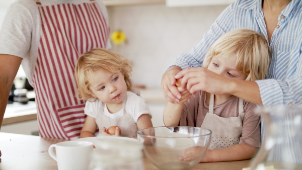 Front view of young family with two small children indoors in kitchen, breaking eggs when cooking. Slow motion.