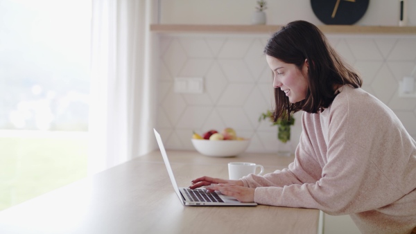 A young woman standing in kitchen indoors at home using laptop computer.