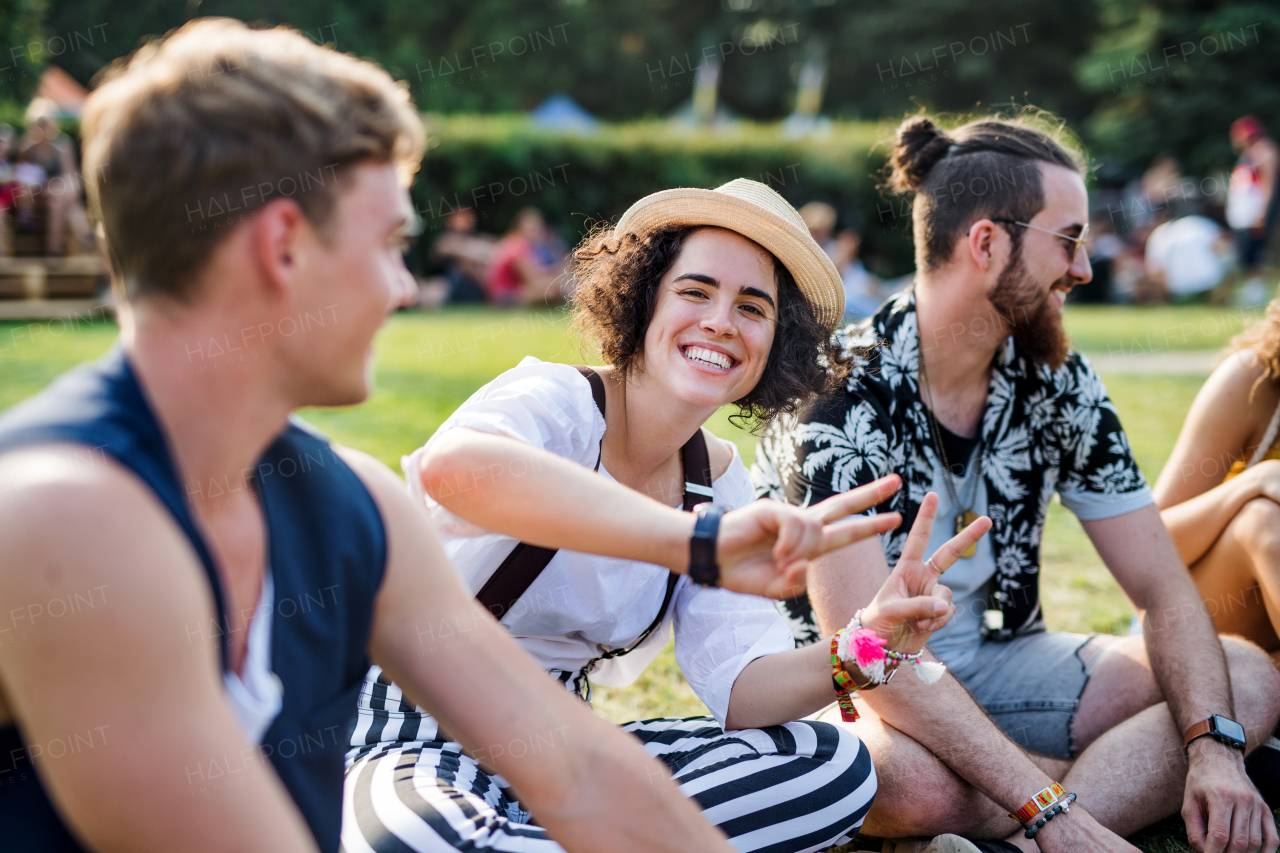 Group of cheerful young friends sitting on ground at summer festival, talking.