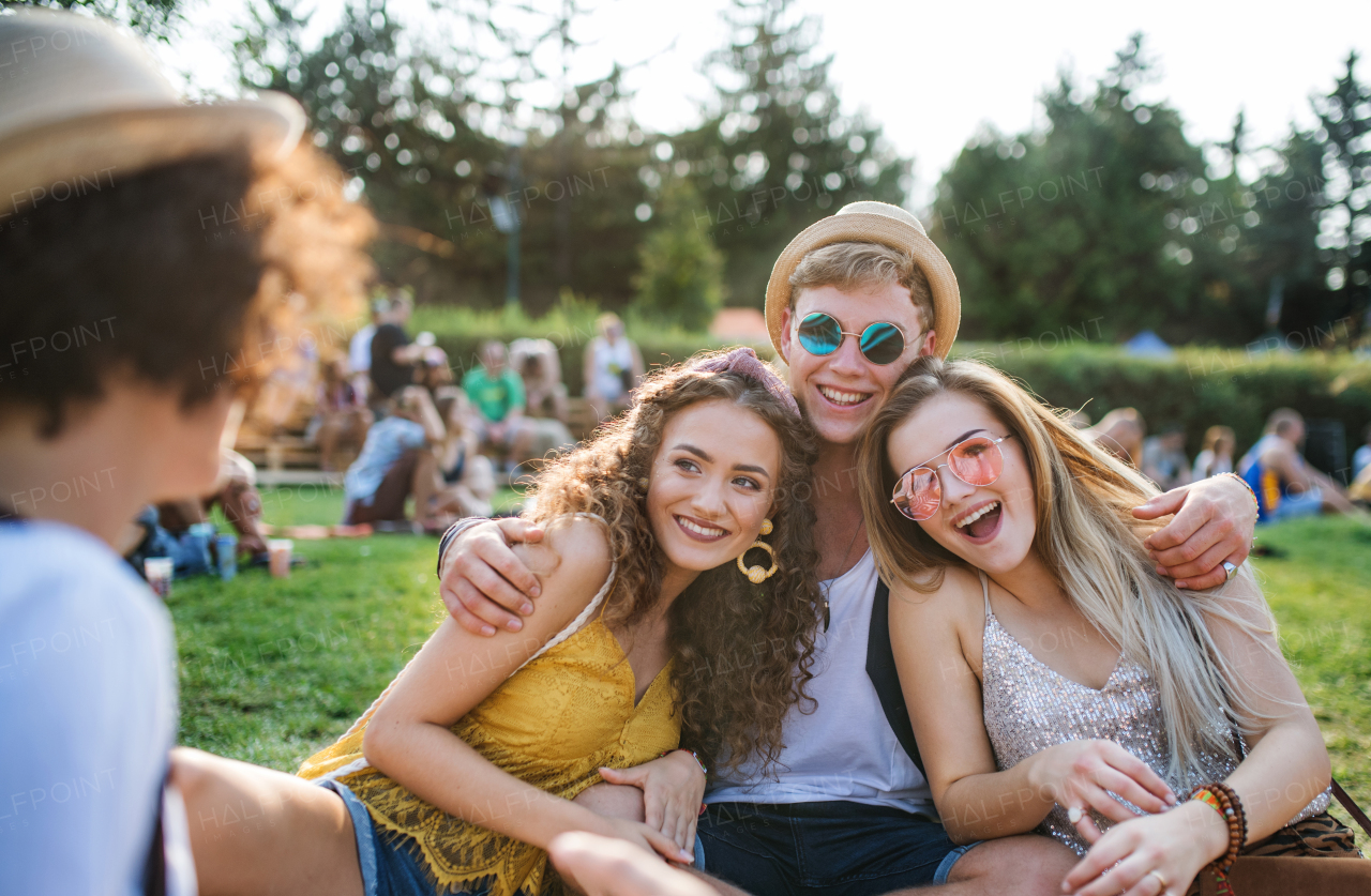 Group of cheerful young friends sitting on ground at summer festival, having fun.