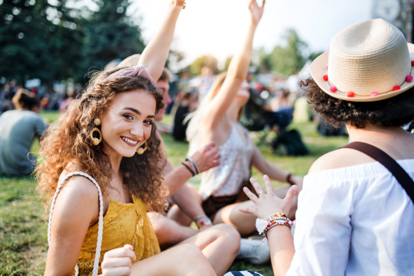 Group of cheerful young friends sitting on ground at summer festival, looking at camera.