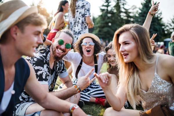 Group of cheerful young friends sitting on ground at summer festival, talking.