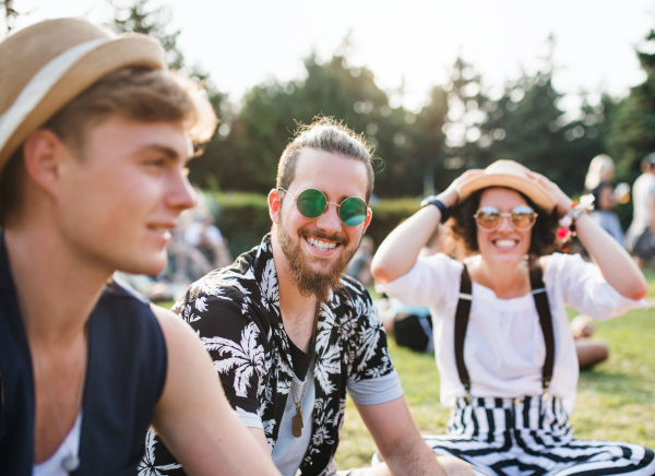 Group of cheerful young friends sitting on ground at summer festival, talking.