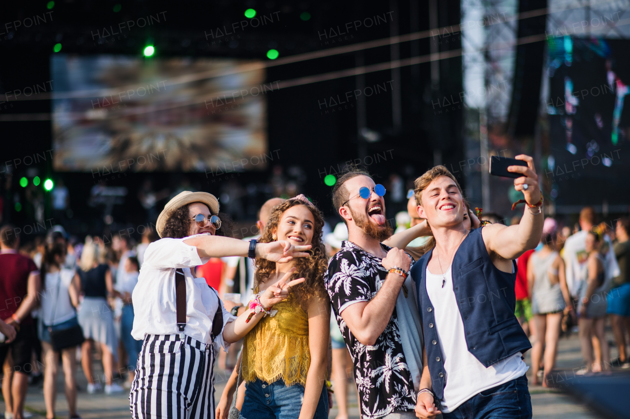 Front view of group of young friends with smartphone at summer festival, taking selfie.