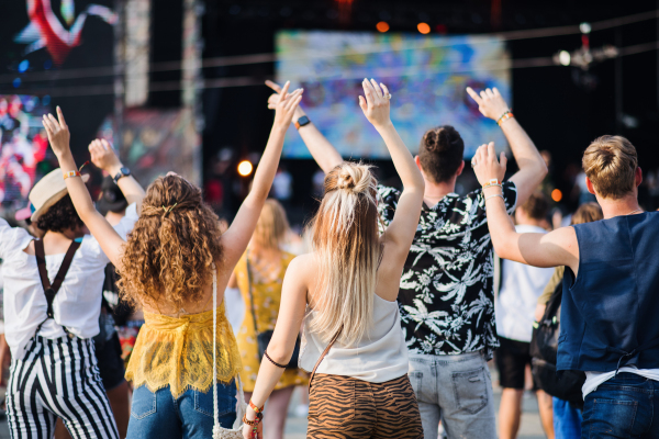 Rear view of group of unrecognizable young friends dancing at summer festival.