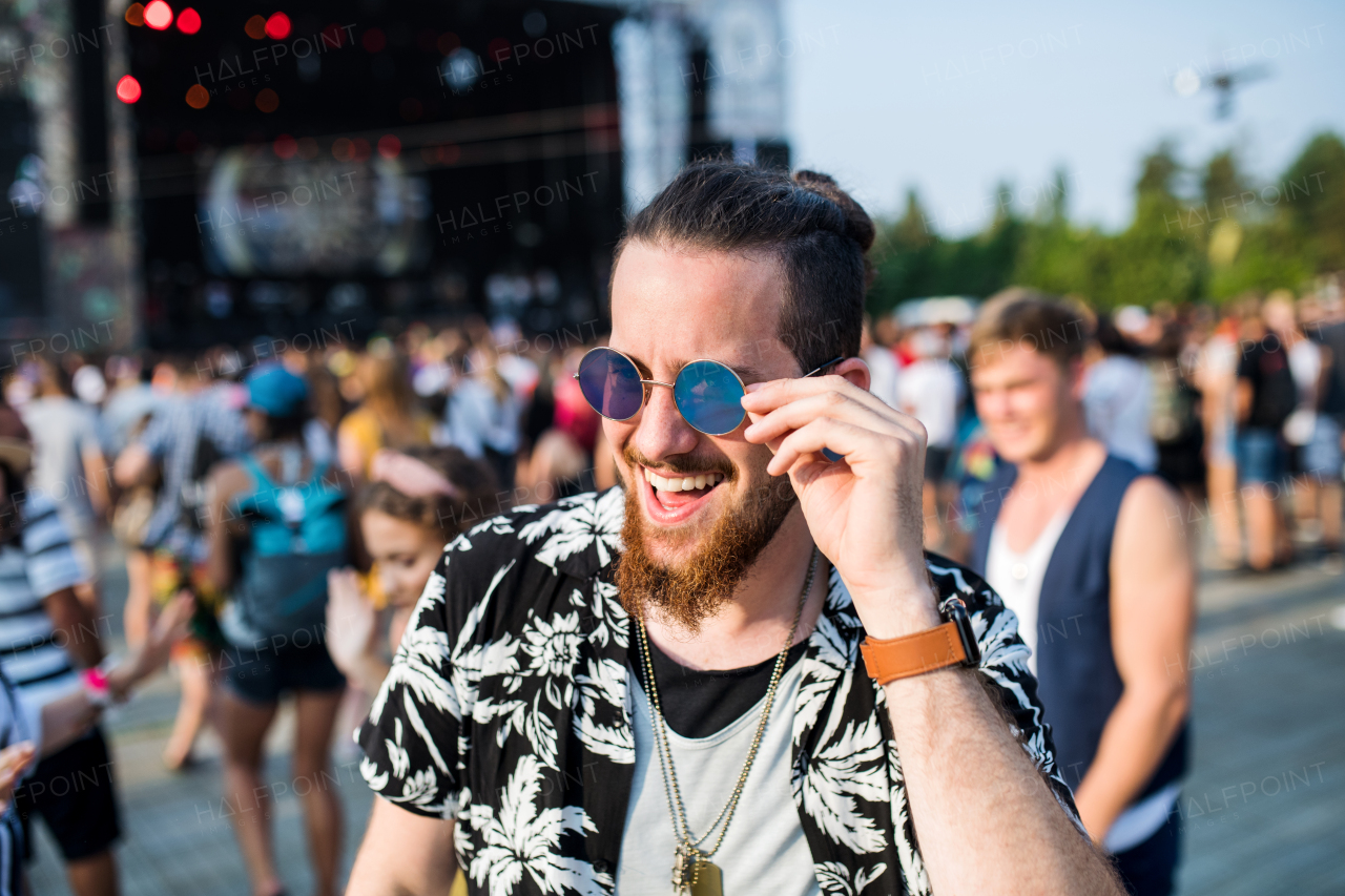 Front view of young man with sunglasses at summer festival, walking.