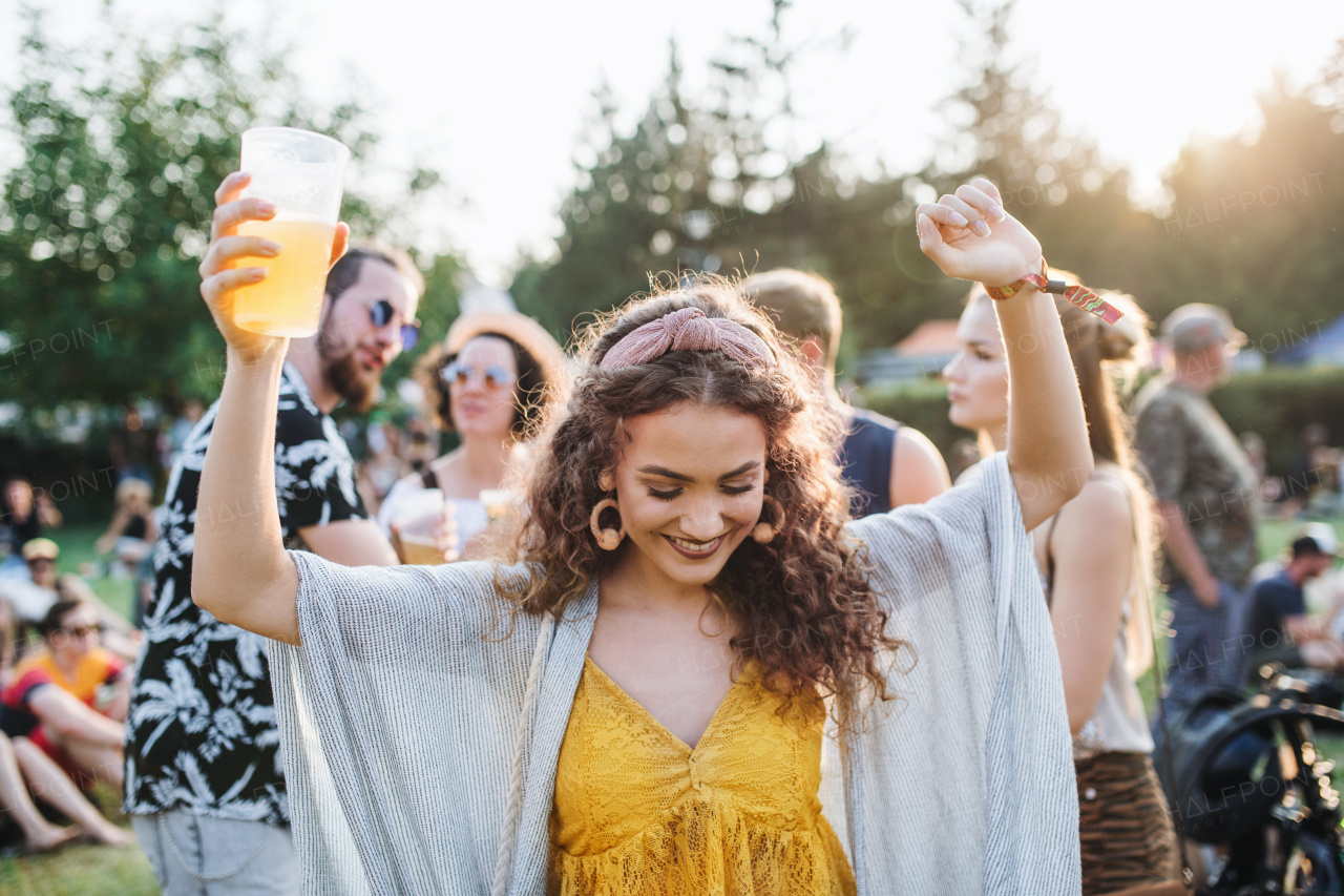 A front view of young woman with drink dancing at summer festival.