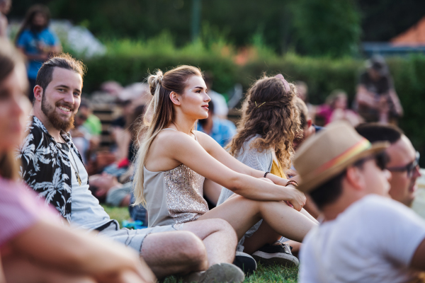 A group of cheerful young friends sitting on ground at summer festival.