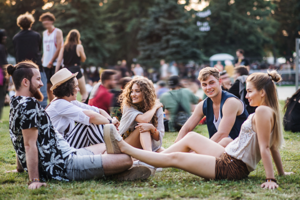 Group of cheerful young friends sitting on ground at summer festival.