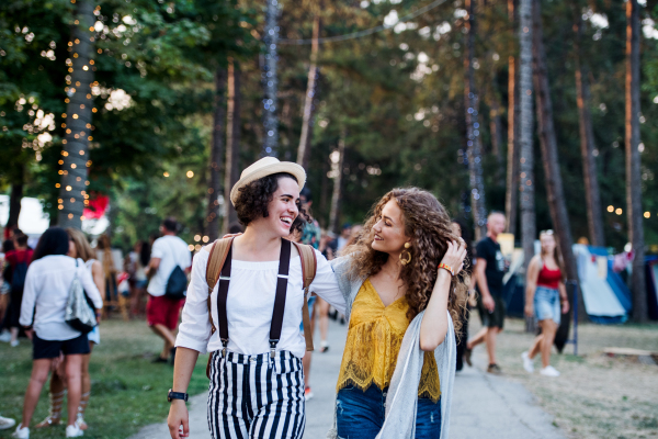 Portrait of two cheerful young women friends at summer festival, walking.