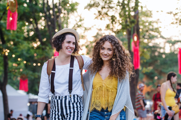 Portrait of two cheerful young women friends at summer festival, walking.